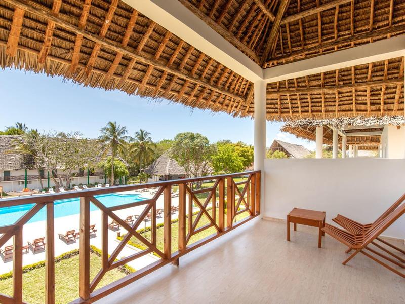Balkon mit Holzgeländer und Liegestühlen mit Blick auf einen Pool und Palmen.