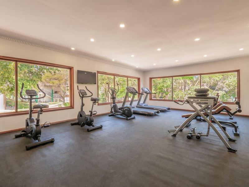 Moderner Fitnessraum mit verschiedenen Trainingsgeräten und großen Fenstern mit Blick ins Grüne.