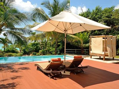 Zwei Liegestühle unter einem Sonnenschirm neben einem Pool mit Palmen im Hintergrund.
