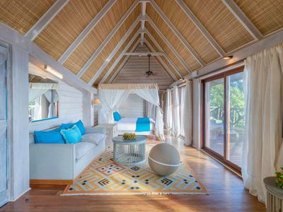 Helles Wohnzimmer mit Holzboden, weißen Möbeln und großen Fenstern mit Vorhängen.