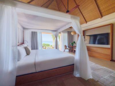 Ein Hotelzimmer mit Himmelbett, Holzboden und Meerblick durch große Fenster.