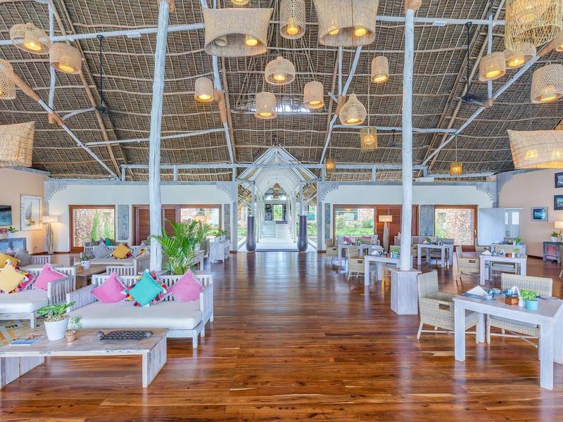 Großer heller Raum mit Holzboden, weißen Sofas, bunten Kissen und hohen Deckenlampen.