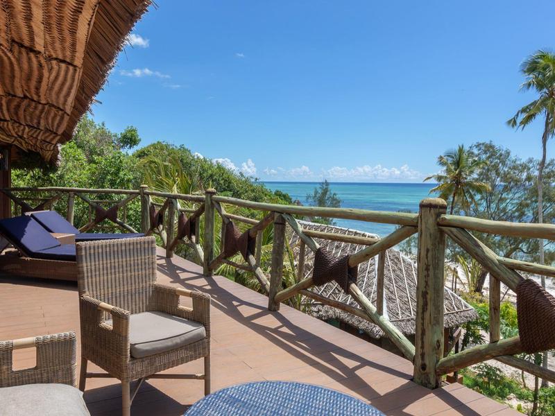 Balkon mit Holzgeländer, Stühlen, Hängematte und Ausblick auf tropisches Meer und Palmen.