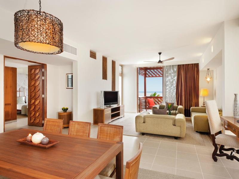 Heller, moderner Wohn- und Essbereich mit Holzmöbeln, cremefarbenem Sofa und großen Fenstern.