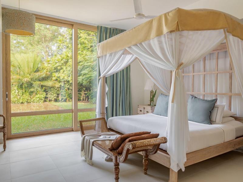 Helles Schlafzimmer mit Himmelbett, weißer Bettwäsche, Holzmöbeln und großem Fenster zum Garten.