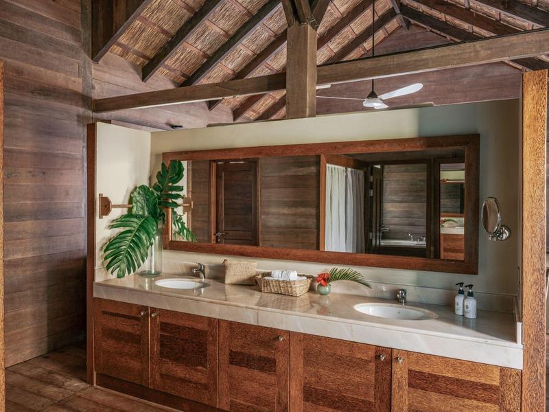 Großes Badezimmer mit Holzdecke, Doppelwaschbecken, großem Spiegel und Pflanzen auf der Arbeitsfläche.