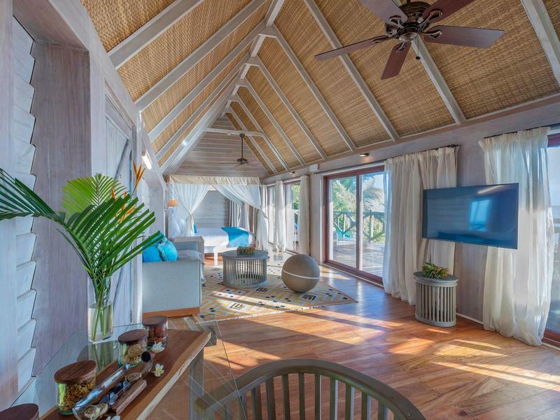 Geräumiges Wohnzimmer mit Holzboden, großen Fenstern, Deckenventilator und moderner Einrichtung.