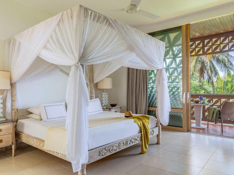 Großes Schlafzimmer mit Himmelbett, weißen Vorhängen und Zugang zu einem Balkon mit Palmenblick.
