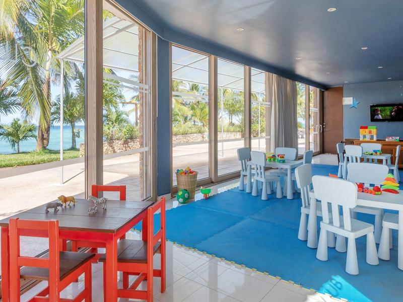 Zimmer mit zwei Himmelbetten, Deckenventilator, Fernseher und Balkon mit Blick auf Palmen.