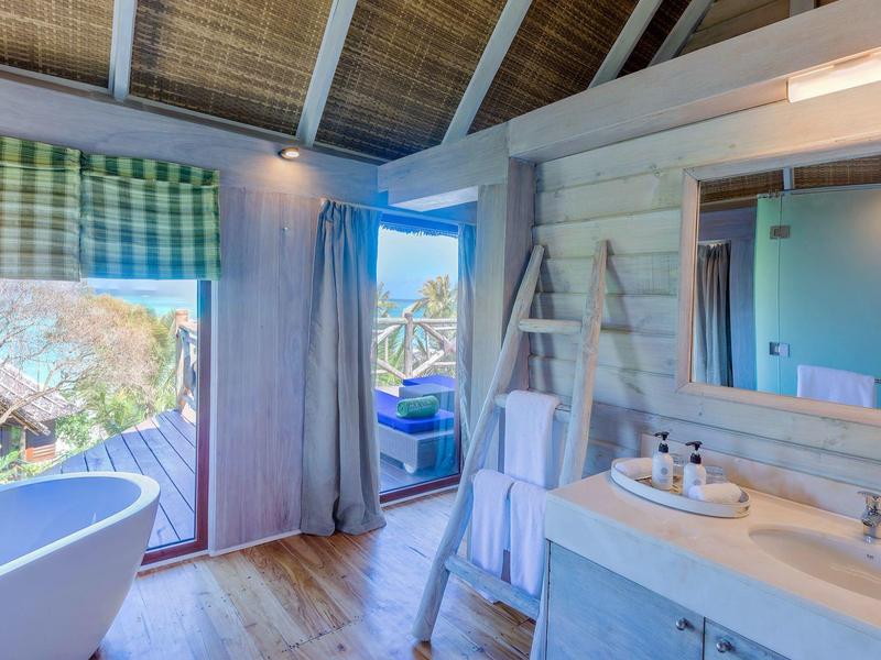 Helles Badezimmer mit freistehender Badewanne, Holzdecken, großem Spiegel und Blick auf Terrasse.