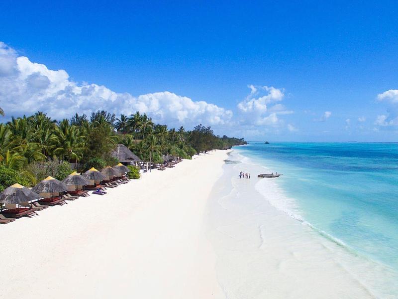 Balkon mit hölzernem Geländer, Tisch mit Flaschen und Stühlen, grüne Palmen und blauer Himmel im Hintergrund.
