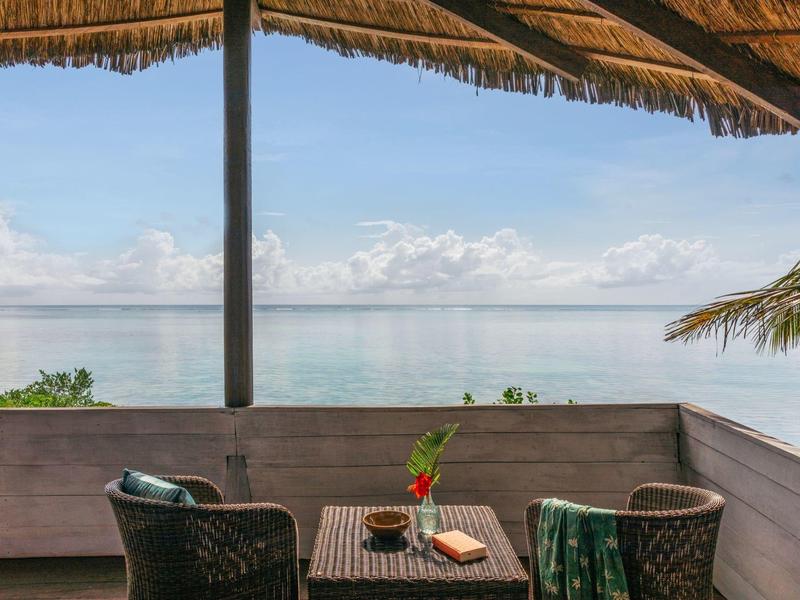 Balkon mit zwei Stühlen, Tisch, Pflanzen und Blick auf ruhiges Meer unter blauem Himmel.