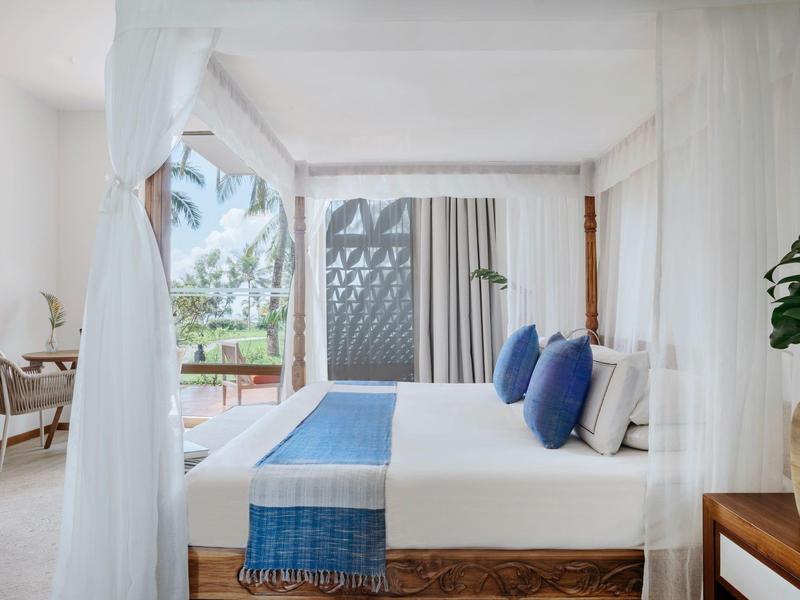 Helles Schlafzimmer mit großem Bett, blauem Läufer, weißen Vorhängen und Zugang zu Balkon.