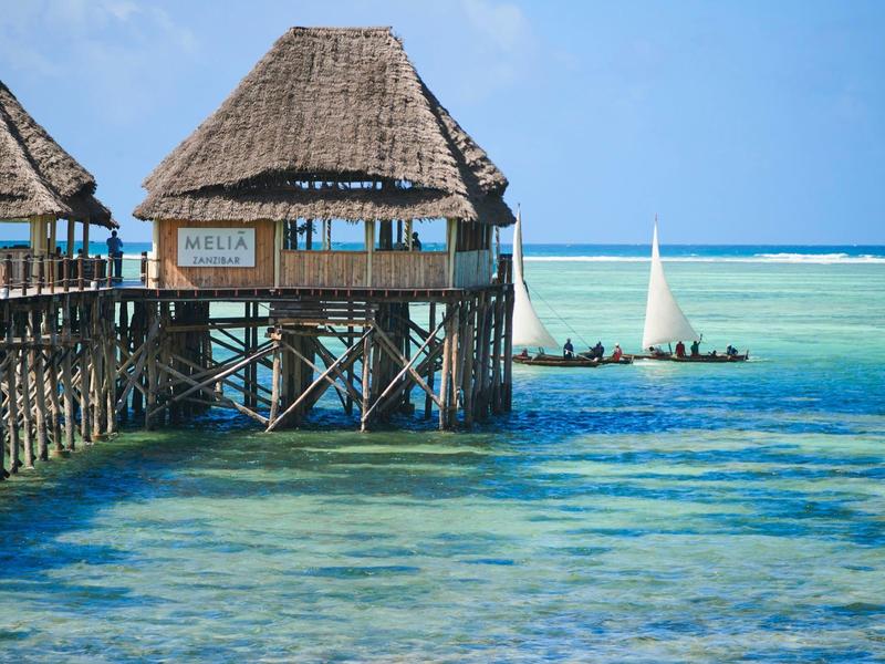 Über dem klaren, türkisfarbenen Meer ragen Bambushäuser mit Strohdächern auf Stelzen.