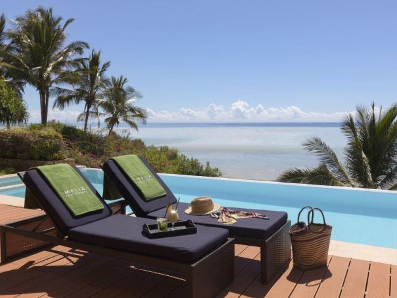 Zwei Liegestühle am Pool mit Handtüchern, Palmen und Meerblick bei klarem Himmel.