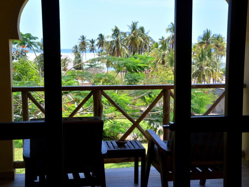 Blick von einem schattigen Balkon mit Stühlen auf eine grüne tropische Landschaft und Palmen.
