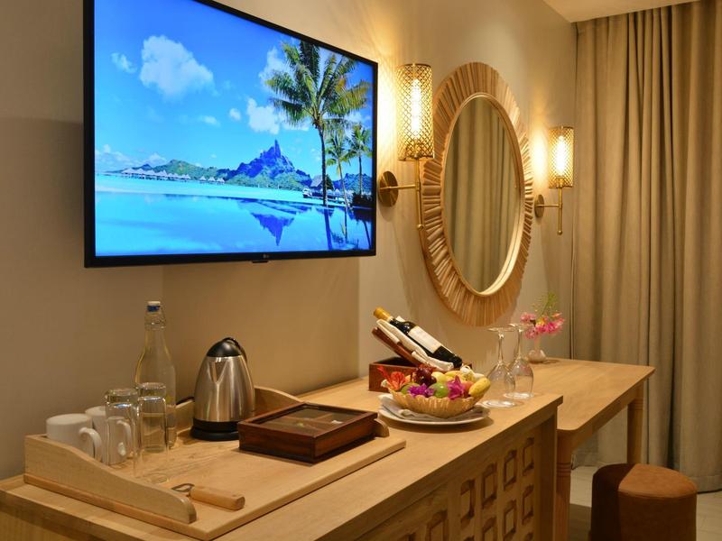 Elegantes Hotelzimmer mit Wandfernseher, Spiegel und Snackstation auf Holzkommode.