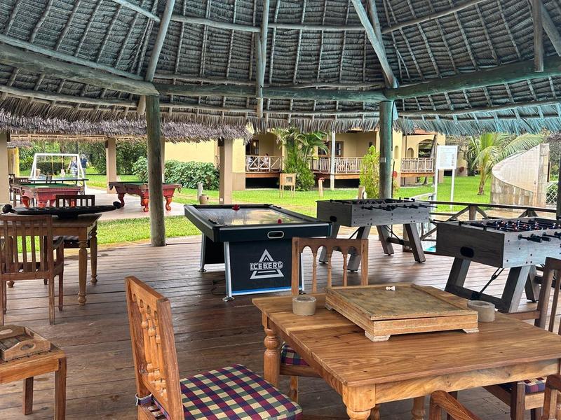 Offener Pavillon mit Holzmöbeln und Billardtisch in grüner Hotelumgebung.