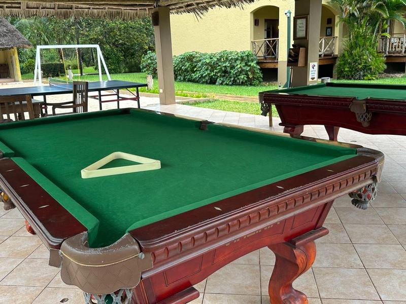 Freiluftbereich mit Billardtischen unter Überdachung neben Wohngebäuden.