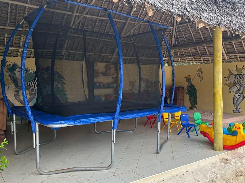 Überdachter Bereich mit Trampolin, Sitzgelegenheiten und buntem Spielzeug, gelbe Wände, Strohdach