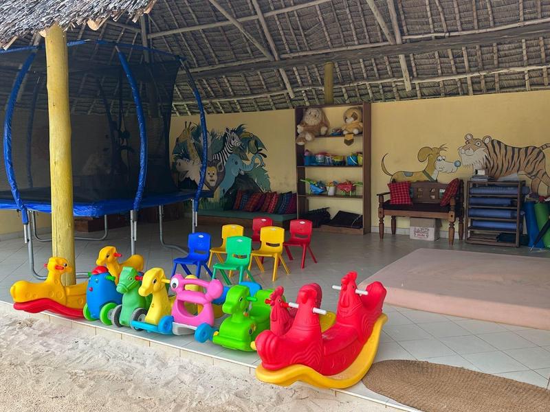 Bunte Kinderspielgeräte unter einem überdachten Bereich neben einer Sitzgruppe