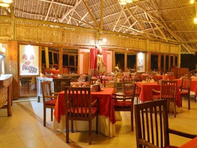 Gemütliches Restaurant mit roten Tischtüchern und Holzstühlen unter einem hohen Strohdach.