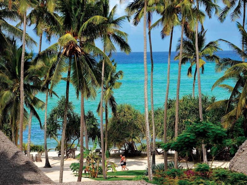 Tropischer Strand mit Palmen, weißem Sand und klarem türkisfarbenem Wasser an einem sonnigen Tag.