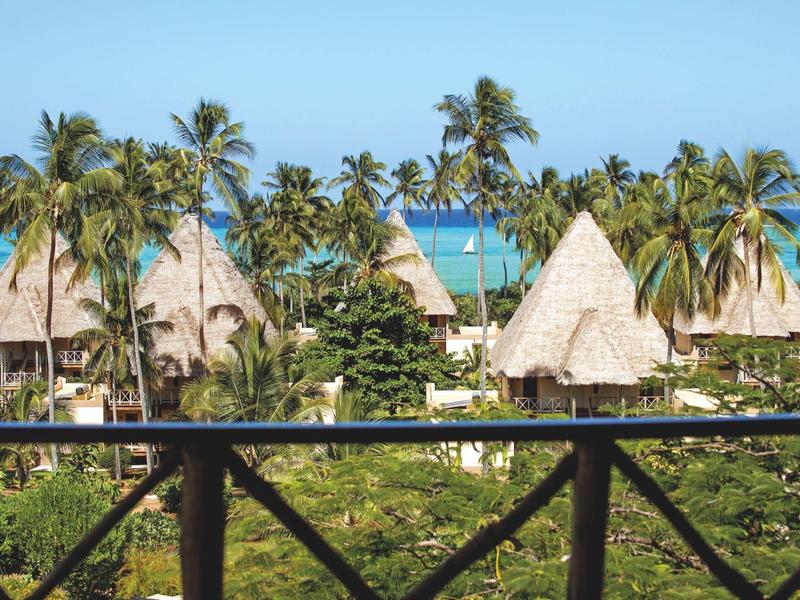 Blick auf palmengesäumte Strohdachhütten und das Meer in einem tropischen Urlaubsort.