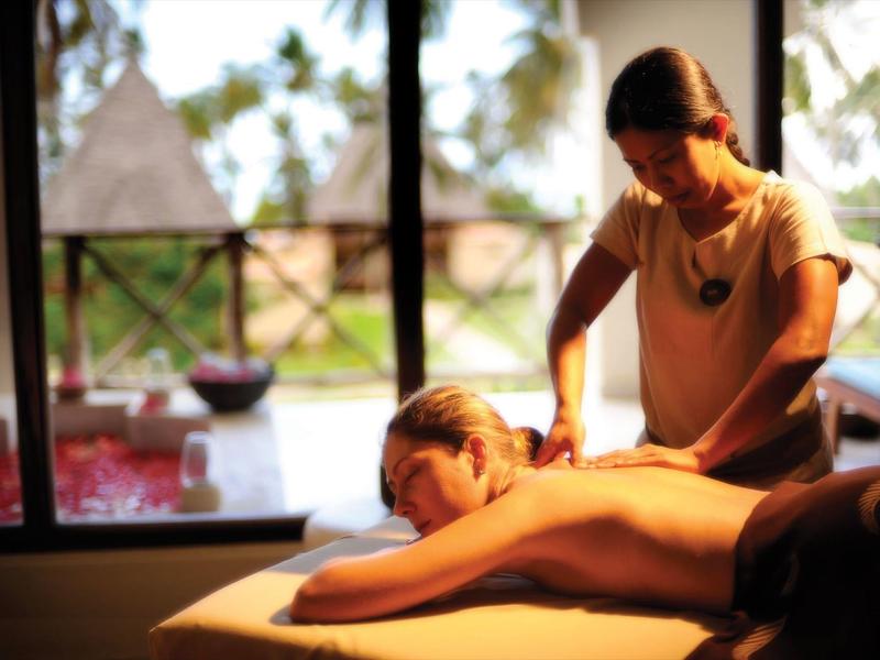 Frau erhält Rückenmassage in hellem Wellnessraum mit Blick auf Garten