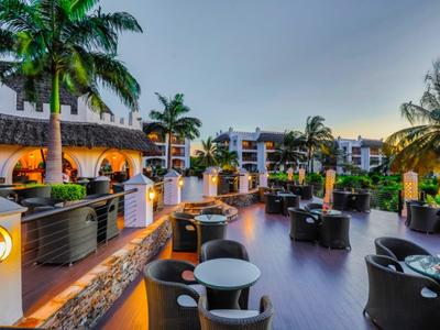 Abendliche Terrasse mit modernen Sitzgruppen, Palmen und Hotelgebäuden im Hintergrund.