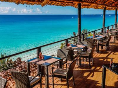 Terrasse mit Tischen und Stühlen mit Blick auf das blaue Meer und den Himmel.