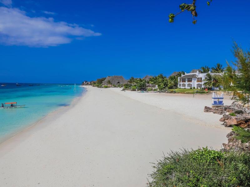 Weißer Sandstrand mit klarem türkisfarbenem Wasser und blauem Himmel am sonnigen Tag.