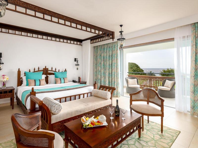 Helles Schlafzimmer mit Holzmöbeln, großer Bett, Sitzbereich und Meerblick durch große Fenster.