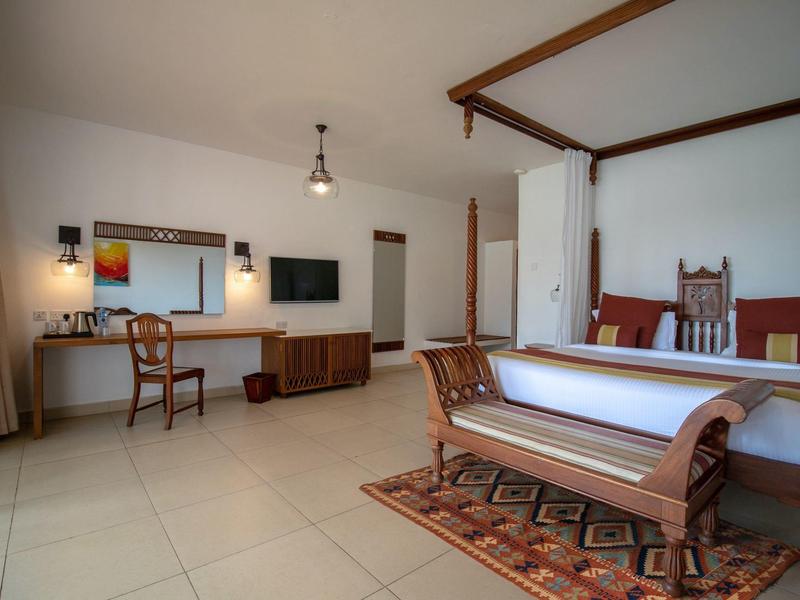 Helles Schlafzimmer mit vierpfostenbett, Spiegel, Fernseher, Schreibtisch und Holzbank auf Teppich.