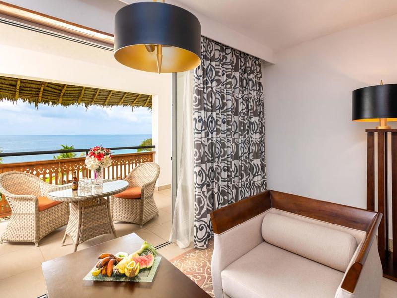 Helle Terrasse mit Korbsesseln, Tisch, Blumen und offenem Blick auf Meer und Himmel.