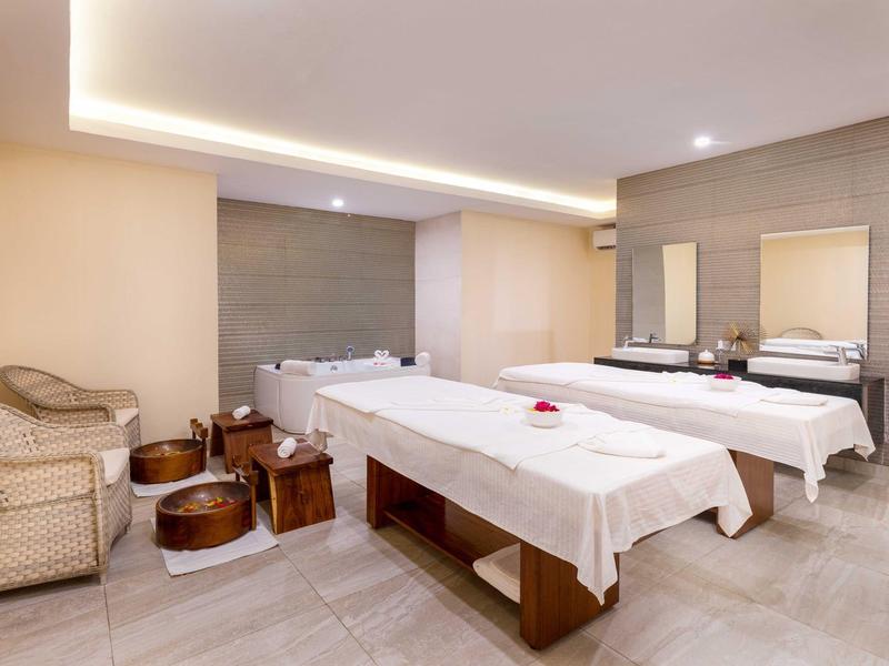 Helles Wellnesszimmer mit zwei Massageliegen, Korbsesseln und Spiegelwand.