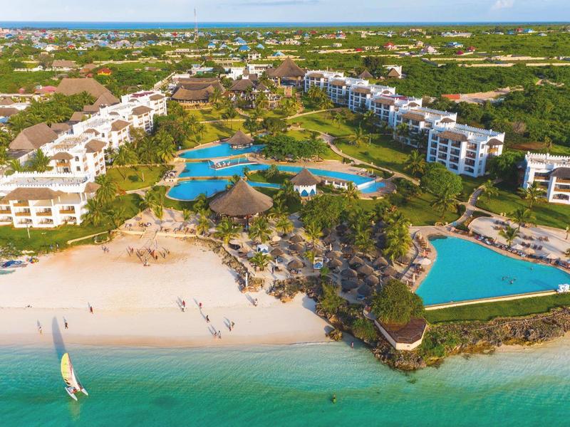 Strandresort mit mehreren Pools, grünen Palmen, weißen Gebäuden und türkisem Meerwasser.