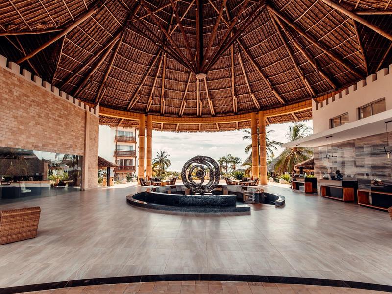 Großer offener Empfangsbereich mit Holzdach, zentralem Brunnen und gemütlichen Sitzgelegenheiten.