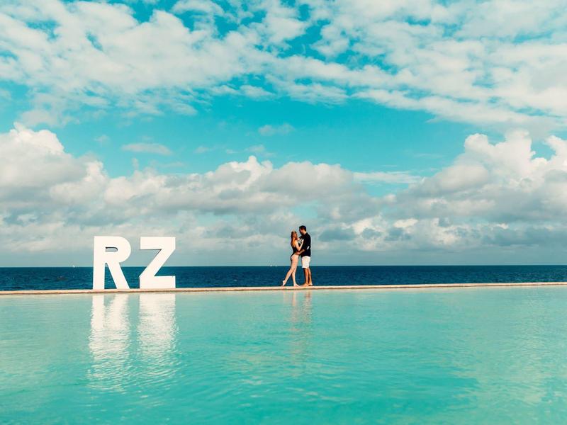 Paar steht am rand eines großen blauen pools mit weißen buchstaben "RZ" und wolkigem himmel.