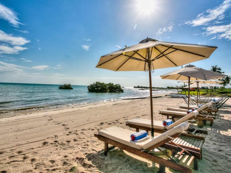 Strand mit Sand, Liegestühlen und Sonnenschirmen unter blauem Himmel mit Sonne.