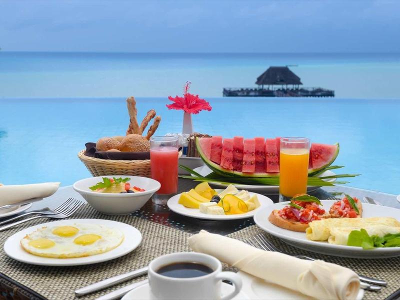 Frühstück mit Kaffee, Obst und Eiern am Pool, Blick auf ruhiges Meer und Insel bei klarem Himmel.
