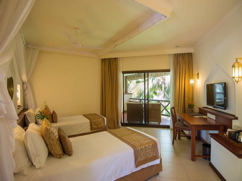 Ein stilvolles Hotelzimmer mit zwei Betten, Schreibtisch, TV und Balkon mit Blick ins Grüne.