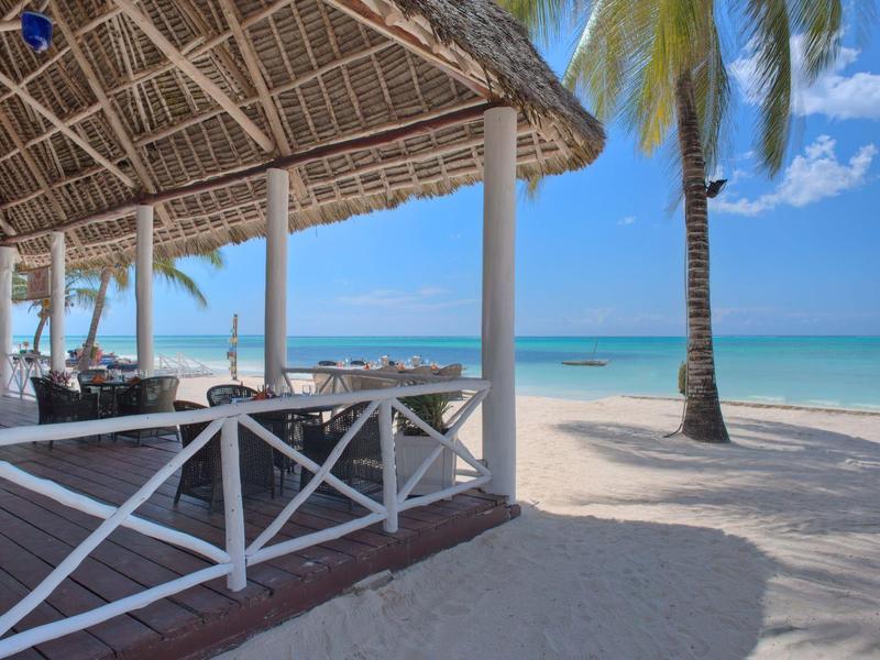 Offener Strandpavillon mit Palmbaum und Blick auf den Ozean bei klarem Himmel.