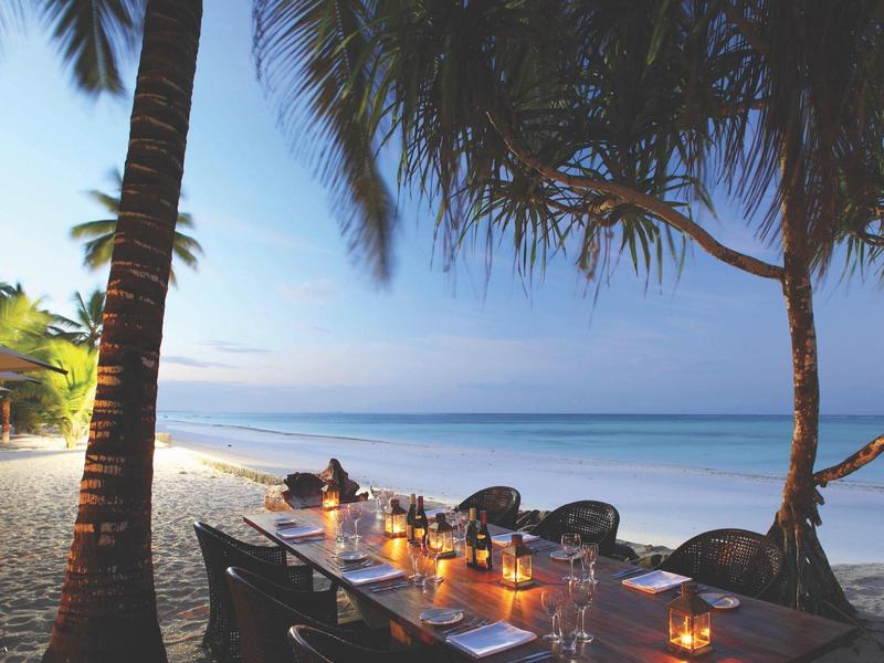 Romantisch beleuchteter Tisch unter Palmen am Strand bei Sonnenuntergang.