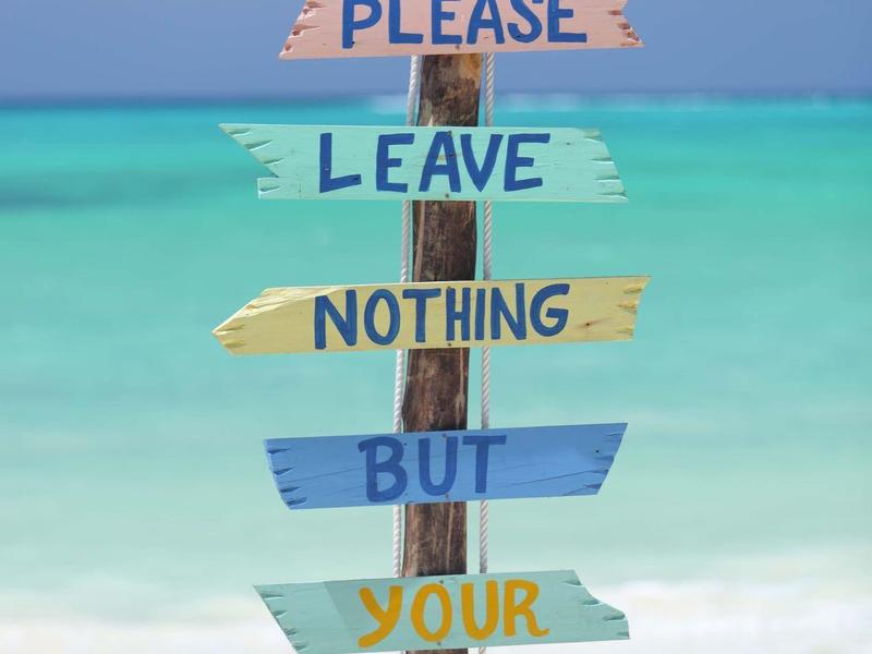 Bunte Holztafel am Strand mit der Aufschrift ‚Please leave nothing but your footprints‘.