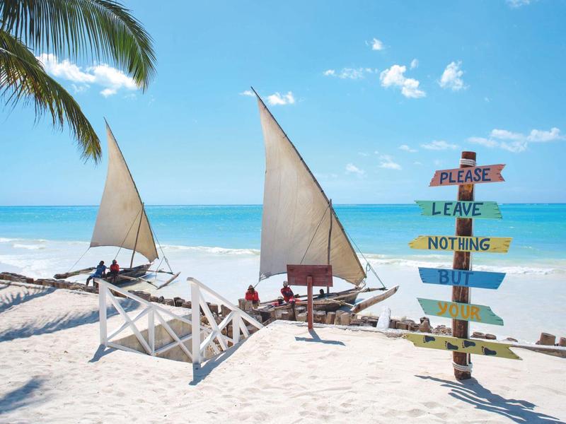 Segelboote am weißen Sandstrand mit buntem Holzschild und Palmen im Hintergrund