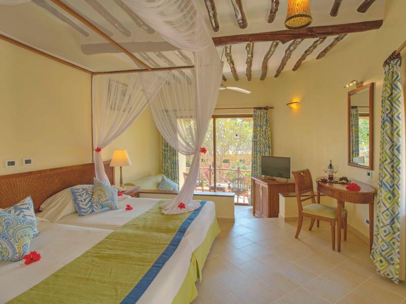 Helles Hotelzimmer mit zwei Betten, Schreibtisch, Stühlen und großen Fenstern mit Vorhängen.