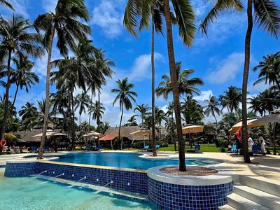 Außenpool mit Palmen und blauen Himmel in einer tropischen Hotelanlage.