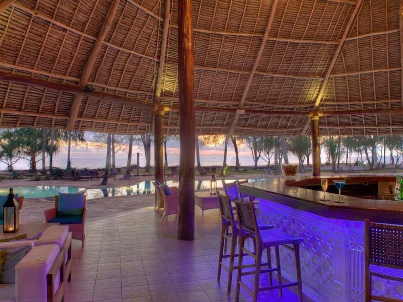 Offene Bar mit Stühlen und gemütlicher Sitzgruppe unter einem Strohdach am Strand