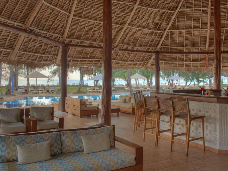 Offener Strandbarbereich mit Strohüberdachung, Barhockern und gemütlichen Sitzgruppen am Sandstrand.